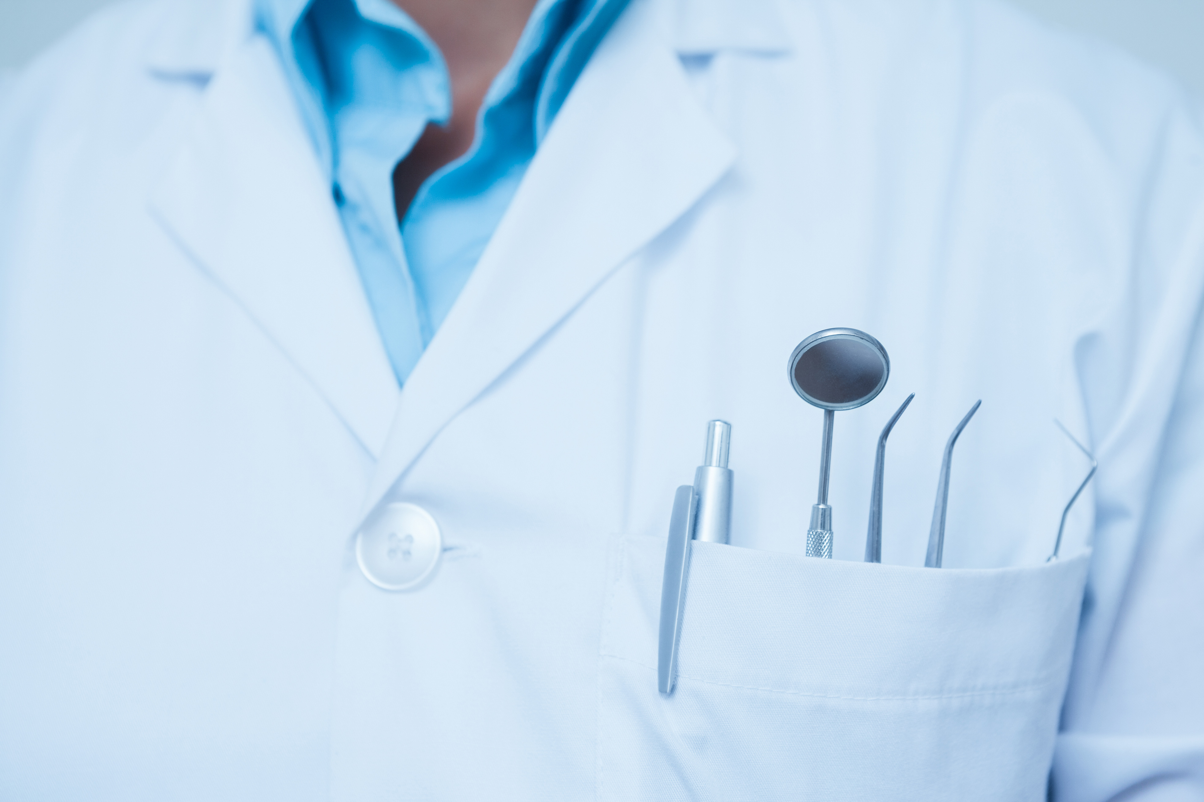 Close-up of dental instruments in a white coat pocket, including a mirror and dental probes.