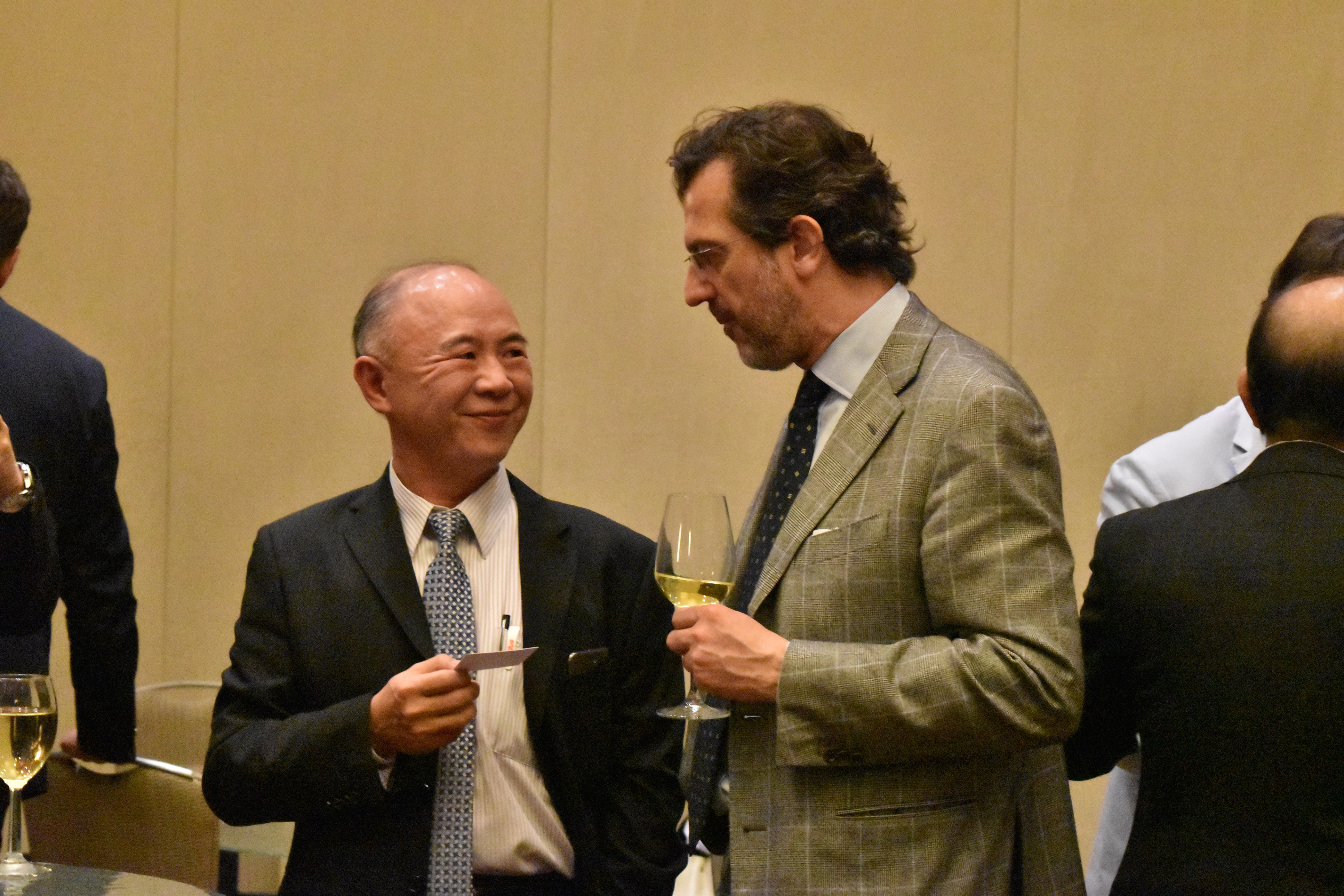 Two professionals talking during an IFED networking event, one holding a glass of wine and the other a business card.